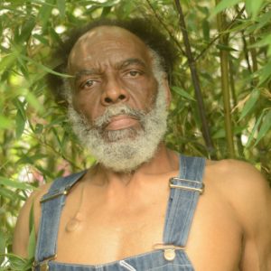 Head shot of poet David Jones. Older black man with receding hairline, full white and gray beard, wearing denim overalls and nothing else.