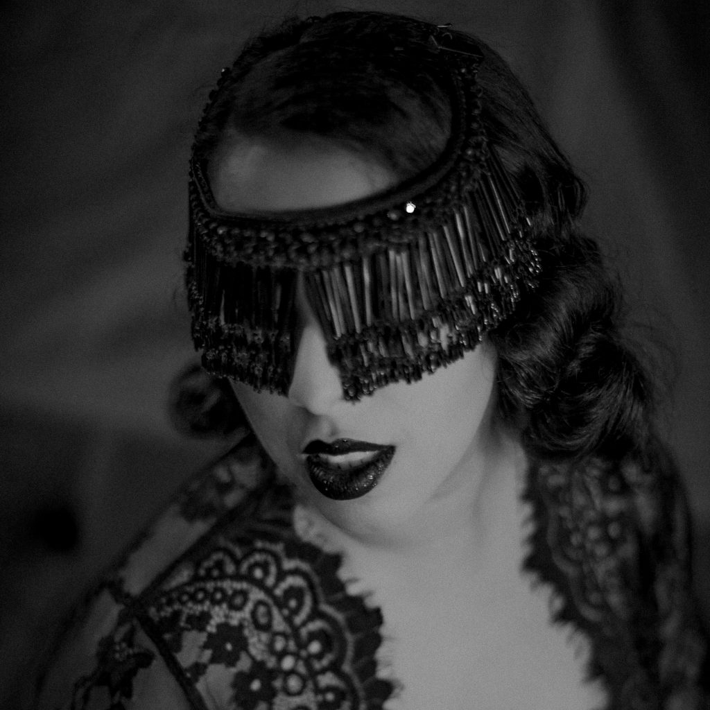 Black and white photo of Carson St. Clair, eyes covered in a beaded blindfold, wearing a lace bolero.