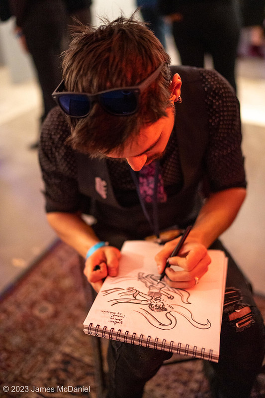 An overhead shot of a person bent over a sketchpad, drawing.
