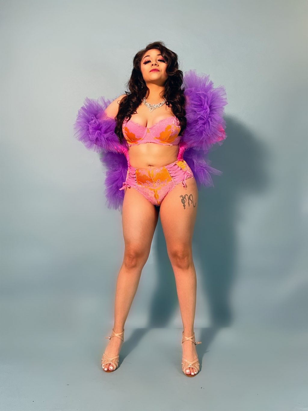 2024 Durational Performers: Camila Sky looking confidently at the camera, full body shot, wearing pink lingerie and a purple boa.