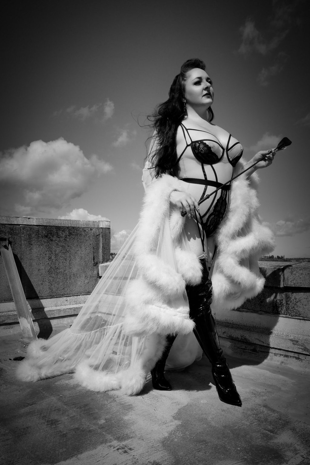 2024 Performance Curators: Icy London sauntering across a rooftop in a maribou robe holding a riding crop.